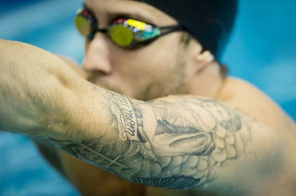 Imágen en primer plano de Lucas Poggi en pileta de natación con antiparras y tatuaje en su brazo.