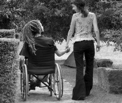 Chico con rastas en silla de ruedas tomado de la mano de su novia, imagen en blanco y negro