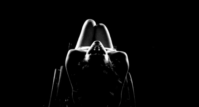 Mujer desnuda recostada sobre su silla de ruedas, imagen en blanco y negro donde se destacan las sombras y contornos