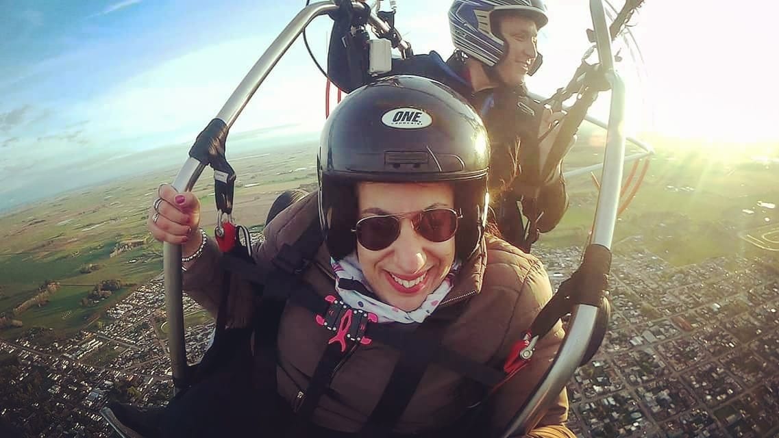Daiana, junto a un instructor, volando en parapente, a muchos metros de altura.